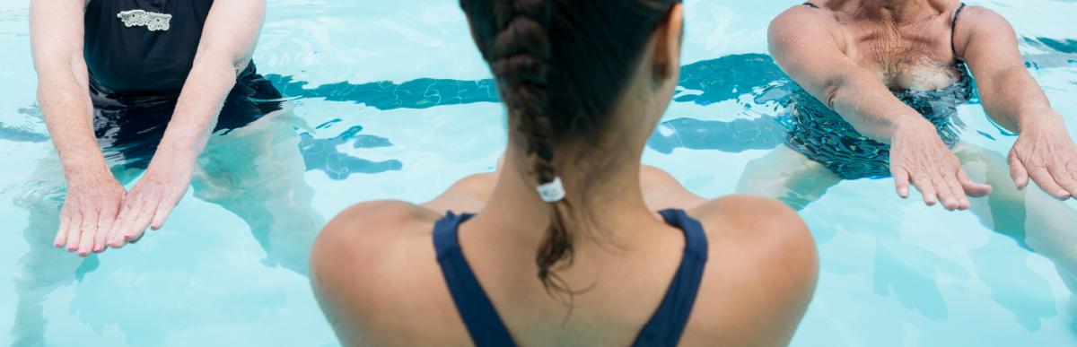Woman swim instructor shown from the back in the pool with two older women students